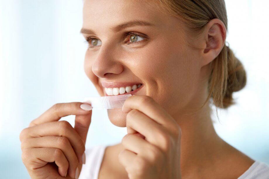 woman applying teeth whitening strips on her teeth